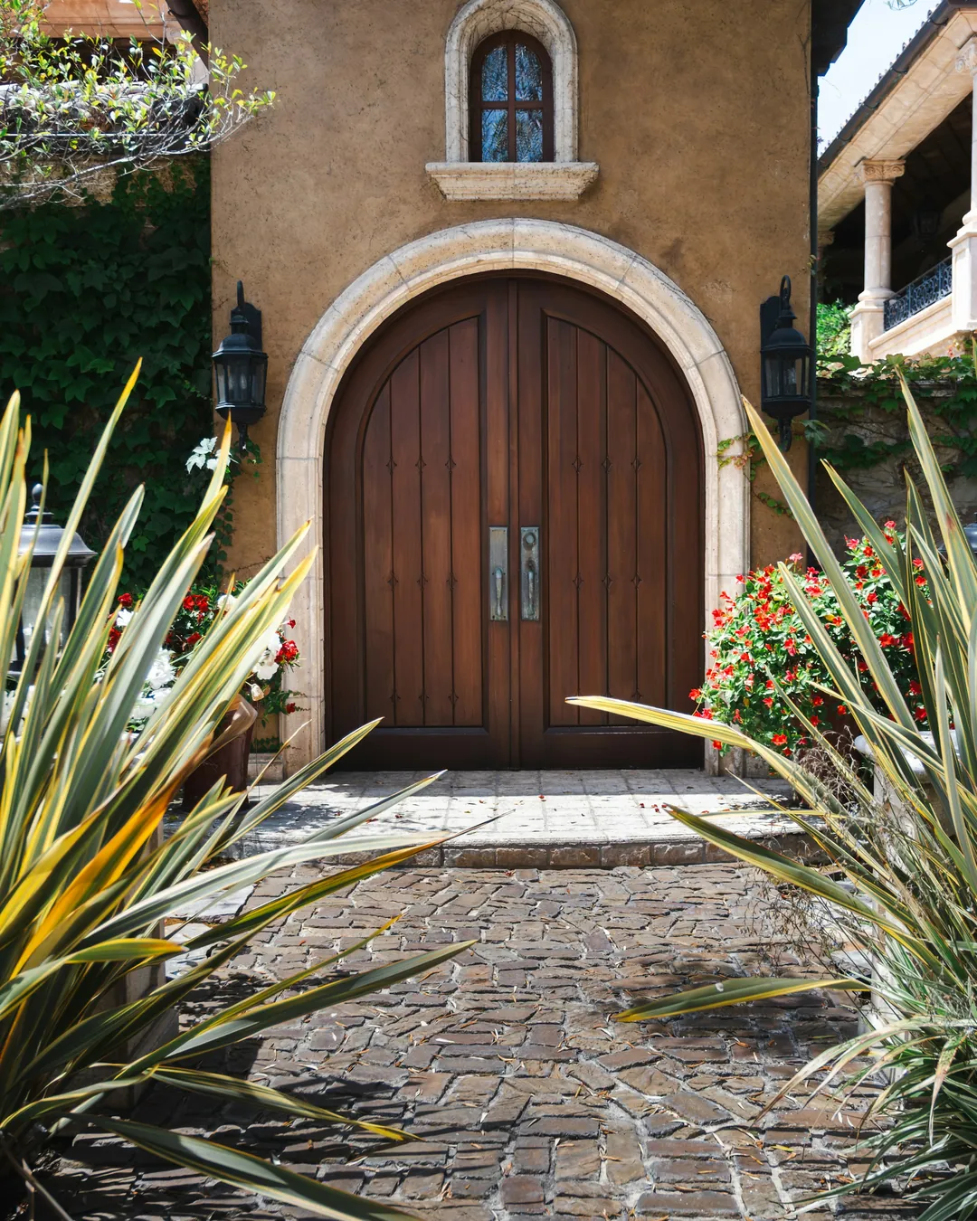 An arched wood front door framed by tropical plants